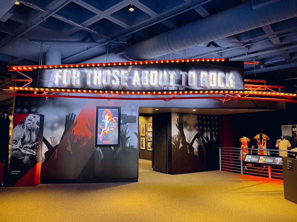 A colorful exhibit at the Rock & Roll Hall of Fame in Cleveland, Ohio features an illuminated sign reading, "For Those About to Rock".