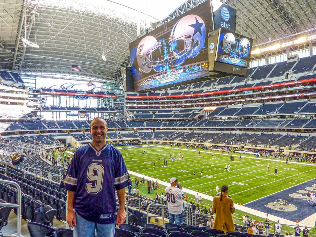 Dan Brewer, of the Ultimate Sports Road Trip blog, stands at his seat in AT&T Stadium for a Cowboys vs Raiders football game on Thanksgiving Day.